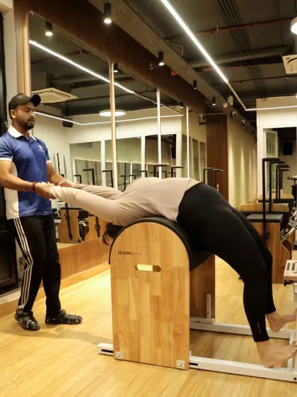 This image shows a coach providing support as a client performs a full-body stretch on the ladder barrel, emphasizing our commitment to safe and effective training.
