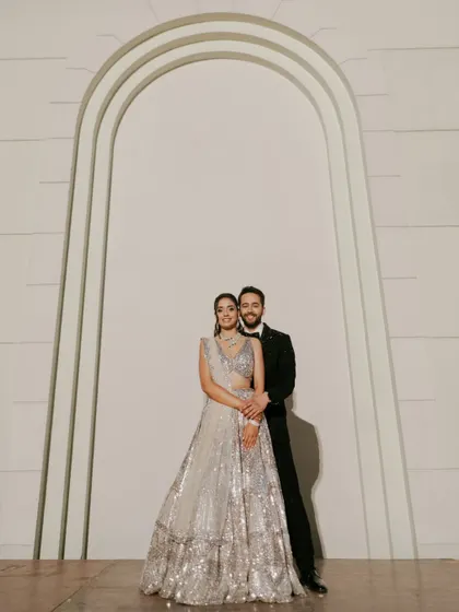 An elegant and classic Sangeet portrait. The couple stands against a minimalist backdrop, letting their stunning outfits and confident connection take center stage.