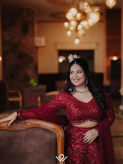 An elegant portrait of a bride in a sparkling red reception lehenga, posing in a warmly lit, classic interior.