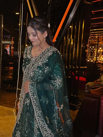This full-length shot shows the complete party look. The soft makeup and elegant hairstyle perfectly complement the richly embroidered green outfit, creating a sophisticated and put-together appearance.
