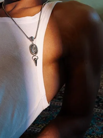 A detailed close-up from the Amama Jewels PhotoVogue series. The focus is on the pendant against the simple white tank top, highlighting the product in a natural setting.