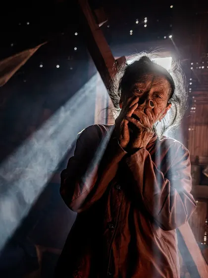 An Apatani woman in Ziro Valley, caught in a ray of light inside her home. This environmental portrait captures her in her daily life, highlighting the unique traditions of her tribe.