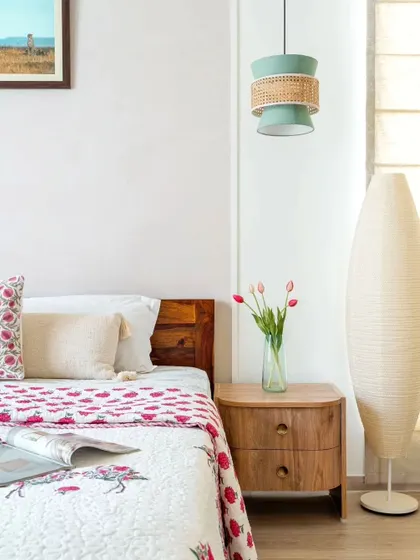 A detail of a bedroom with a unique wicker and mint green pendant light, a paper floor lamp, and floral bedding.
