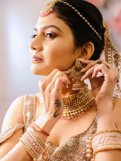 A close-up of the bride getting ready. This shot captures the application of her jewelry, which complements the dewy makeup and subtle glittery eye look.