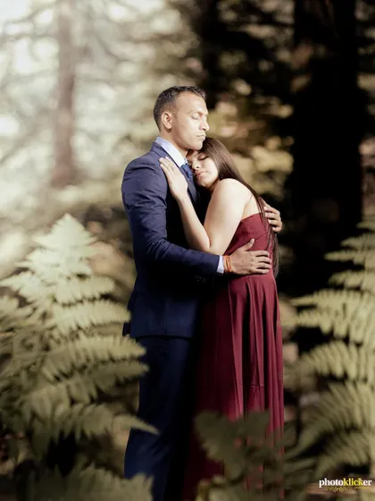 A tender moment as a couple embraces amidst lush green ferns in a forest, creating a soft and romantic portrait.