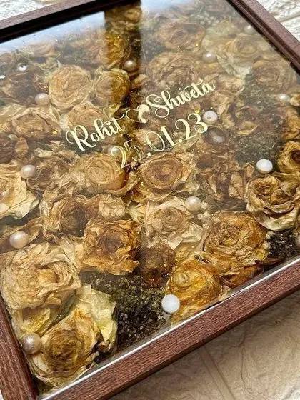 Crafted with love, sealed with resin. This square wooden frame is filled to the brim with preserved varmala flowers, creating a dense and beautiful floral display with the couple's names in the center.