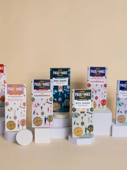 A product lineup of different Paul & Mike chocolate bars, arranged on white blocks for a clean, geometric, and modern look.