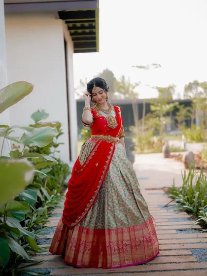 A full-body shot showing the bride walking along a garden path. This captures the flow and movement of the traditional half saree in a natural, elegant way.