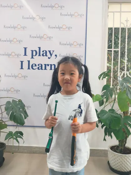 A young girl proudly holds her hammer and screwdriver. I ensure every child, regardless of gender, feels empowered to explore the world of building and engineering.