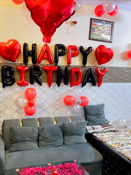 A birthday room decoration with red and black 'Happy Birthday' foil letters and a bed covered in rose petals.