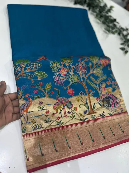A beautiful teal blue Dola Paithani saree, showcasing the rich and detailed artistry of the Paithani weave.