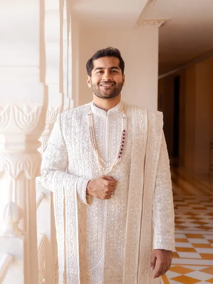 A classic portrait of the groom in his elegant white sherwani, smiling warmly. This shot, taken in a sunlit palace corridor, captures his happiness and regal attire.