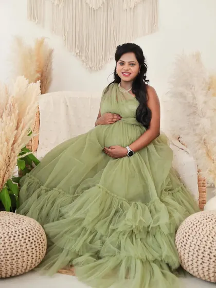 A smiling portrait of a mom-to-be in a light green ruffled gown, seated in our comfortable and stylish boho-themed studio.