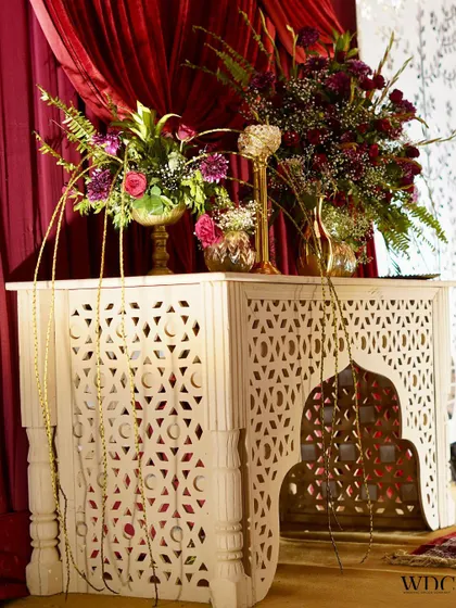An elegant entry piece with red roses and purple blooms. The intricate jali-work console and golden accents set the perfect mood for a royal wedding celebration.