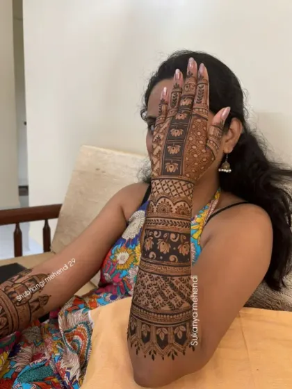 A shy peek from behind a beautifully decorated hand. This full-arm bridal mehendi features intricate bands of traditional patterns, creating a stunning sleeve of henna art.