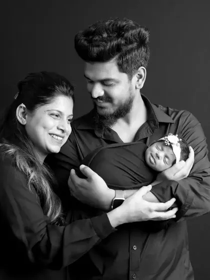 A happy family portrait with both parents and their newborn baby against a classic black backdrop. We guide families into poses that feel natural and showcase their joy and connection.