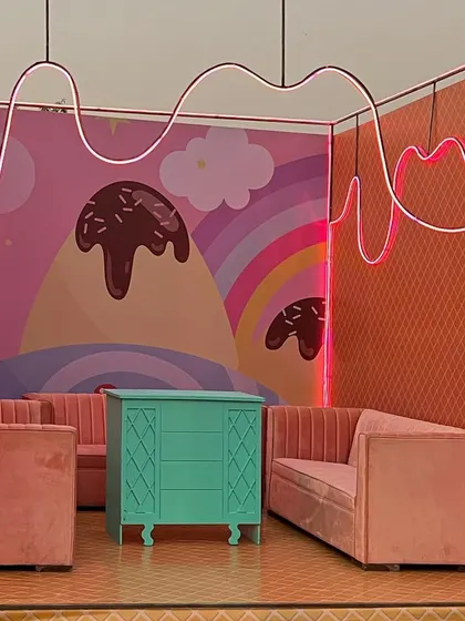 A quirky seating booth inside Candyland, with neon lights mimicking chocolate drizzle and a hand-painted ice cream mountain backdrop.