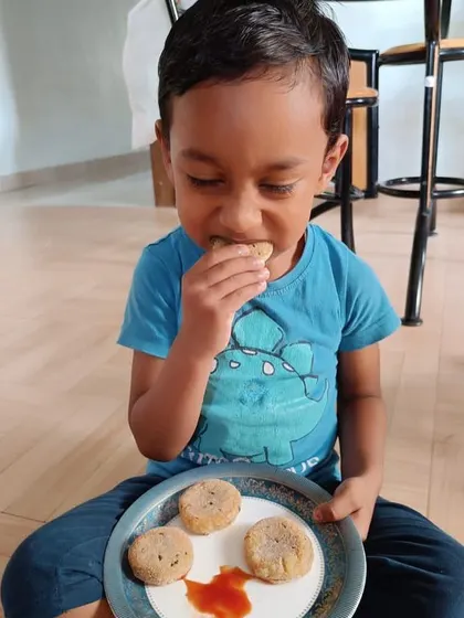 Enjoying the fruits of his labor. This child is eating an aloo tikki he prepared, experiencing the full cycle of work from preparation to enjoyment, which is a core tenet of Montessori education.