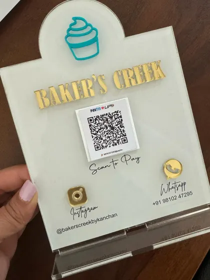 A custom QR code stand for 'Baker's Creek', featuring their brand name in gold lettering and a cute cupcake icon. An essential for any bake sale.