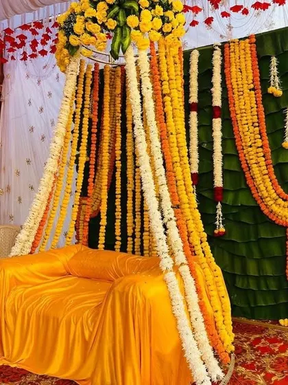 A sofa decorated for a Haldi ceremony with a yellow cover and a canopy of dense marigold and jasmine flower strings.