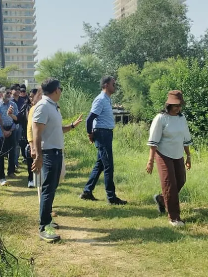 Volunteers walk along a path at Ghata Bundh, with Gurgaon's high-rises in the background, a stark contrast to the green space they are helping to create.