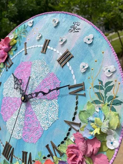 Another detail shot of the pink and blue clock, highlighting the delicate white sculpted flowers scattered across the face.