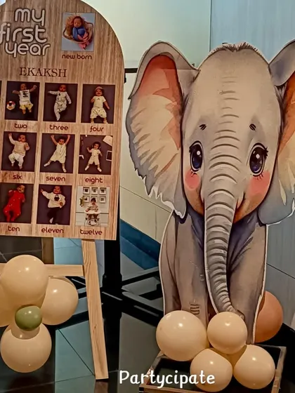 A personalized 'My First Year' milestone board for Ekaksh's safari party. It's a heartwarming display that showcases the baby's growth month by month, accompanied by a cute elephant cutout.