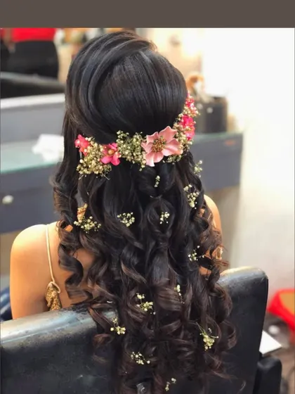 A half-up, half-down hairstyle with voluminous curls and a floral crown, perfect for a sangeet or reception.