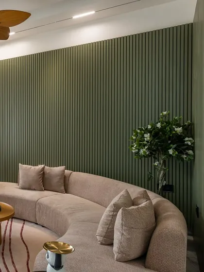 The curved sofa's soft form contrasts beautifully with the rigid vertical lines of the olive green fluted wall. A wooden fan adds a touch of natural warmth to the ceiling.