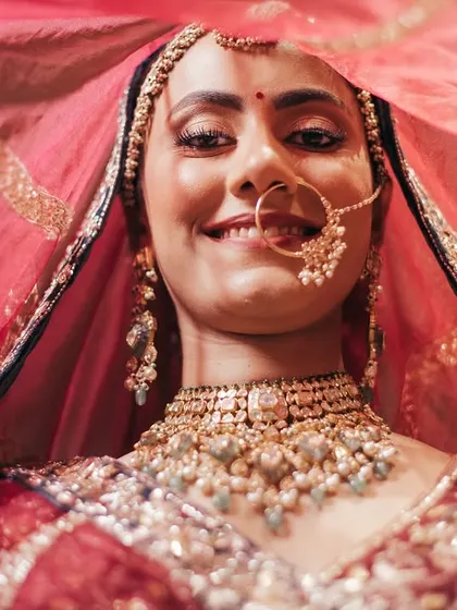 A joyful smile from the bride, Bhavita, from under her veil. This close-up captures her happiness and the intricate details of her bridal look.