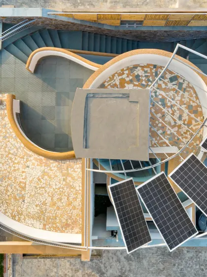 This drone shot captures the intricate design of the rooftop, showing the placement of solar panels, the mosaic-tiled curved surfaces, and the central skylight. The entire roof is a functional system for energy generation and water collection.