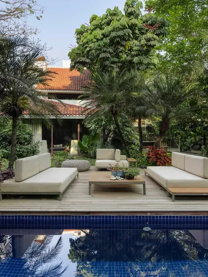 A poolside lounge area set on a timber deck, surrounded by mature palm trees. The symmetrical arrangement of the furniture creates a sense of order and calm, perfect for a resort-style backyard experience.