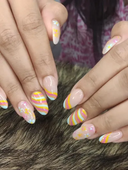 A full view of the playful rainbow stripe and floral nail art on long, oval-shaped extensions.
