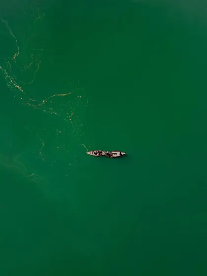 A minimalist top-down view of two boats on the emerald green waters of Naukuchiatal. The simplicity of the composition highlights the peacefulness of the lake and the subtle textures on the water's surface.