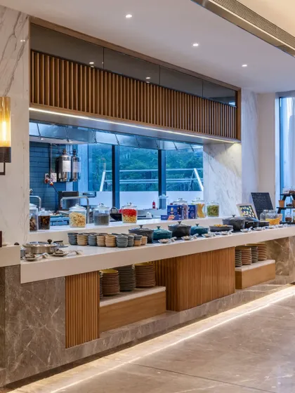 The buffet counter in the restaurant combines warm wood with refined marble. This design choice strikes a balance between minimalism and understated elegance, ensuring both functionality and aesthetic appeal for the dining experience.