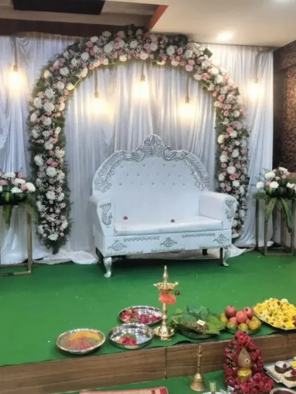 A simple yet elegant baby shower stage with a white floral arch, hanging lights, and traditional lamps (diyas) set up for the ceremony.