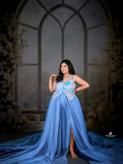 A full-length solo portrait showcasing a beautiful blue gown with a long, sparkling train. The dark, moody backdrop makes the dress and the mom-to-be truly stand out.