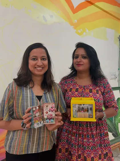 Two participants proudly holding the miniature food scenes they created in a workshop.