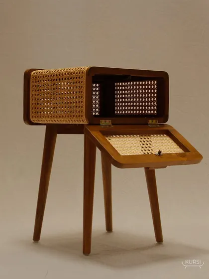 The 'Koshi' table with its top compartment open, revealing the thoughtful storage design and the beautiful contrast of teak and rattan.