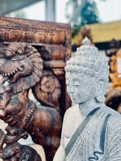 A close-up of a stone Buddha sculpture next to a traditional wooden carved pillar.