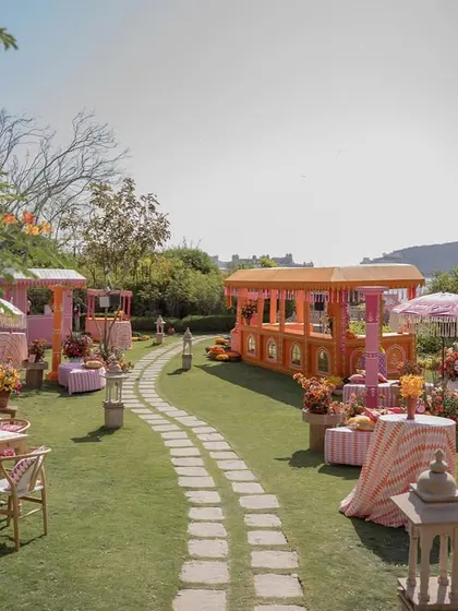A winding stone path through the 'Pyaar ka Pind' setup, leading guests past colorful food stalls and seating areas, all with a view of the lake.