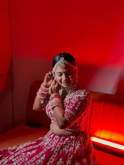 A candid moment of the bride adjusting her earring, captured under dramatic red lighting for her Varmala ceremony.