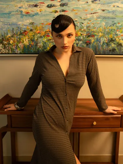 A confident and powerful pose against a clean, architectural background. The lighting highlights the model's form and the texture of the dress.