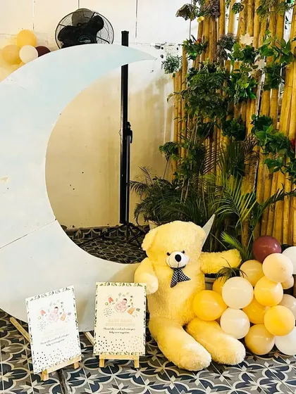 A simple and charming photo corner for a baby shower, featuring a large crescent moon prop and a teddy bear.