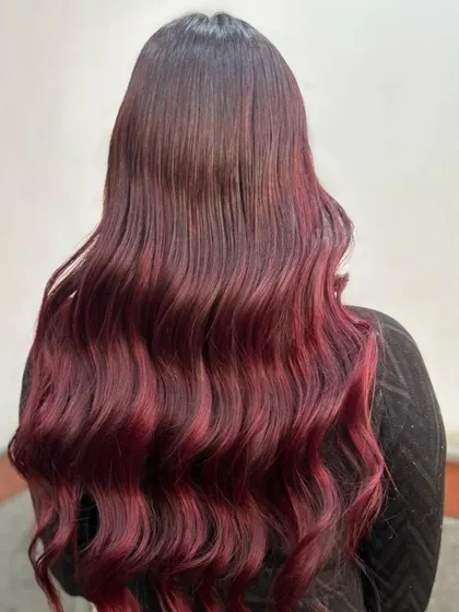 A stunning example of a red and burgundy color melt. The colors transition seamlessly into each other, creating a rich, dimensional look on long, wavy hair.