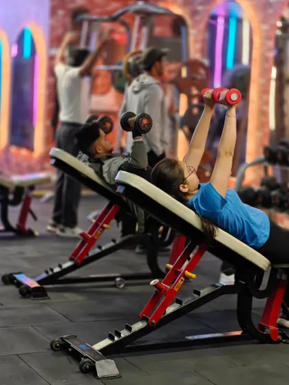 Two clients perform incline dumbbell presses side-by-side. The shared energy in the gym motivates everyone to work harder and stay consistent.