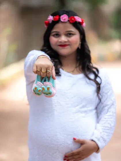 A sweet and simple outdoor portrait. The mom-to-be is holding up a tiny pair of bunny-themed baby shoes, a cute way to announce their coming arrival.
