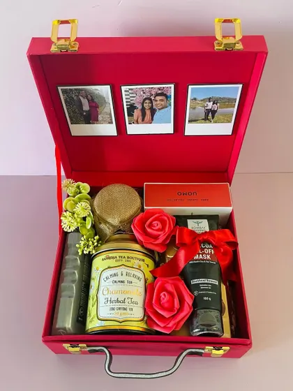 This red suitcase box is curated with a mix of self-care and gourmet items. It includes chamomile tea, a face mask, and chocolates, with polaroid photos for a personal touch.