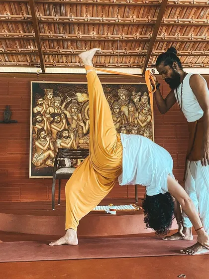 I assist a student in Eka Pada Sirsasana (Foot-behind-the-Head Pose), a deep hip-opening posture. This level of practice is approached with great care, patience, and an understanding of anatomy.