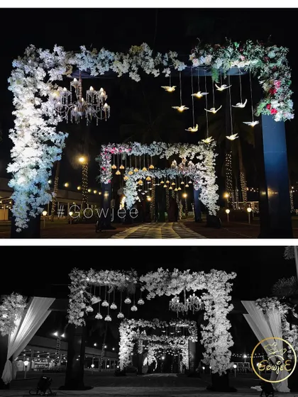 A beautiful floral entrance arch decorated with hanging bird motifs and chandeliers.